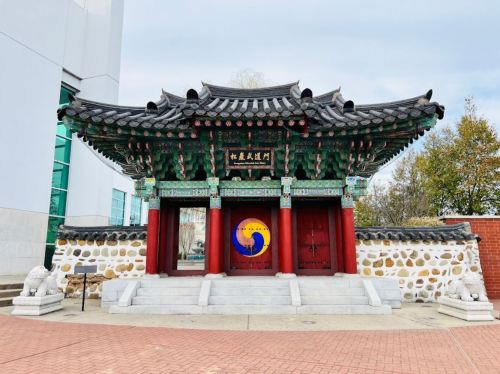 Traditional Korean gate with ornate roof and colorful decorations, set against a stone wall and modern buildings.