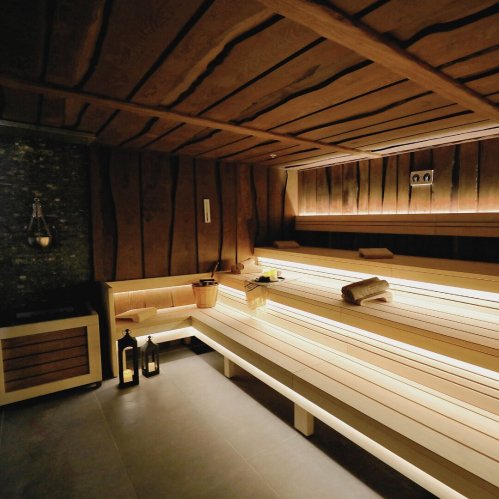 A cozy sauna with wooden benches, soft lighting, and a stone wall, creating a relaxing atmosphere.