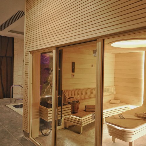 A modern wooden sauna with a bench inside, illuminated by soft lighting, set in a sleek indoor space.