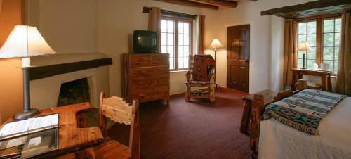 Cozy room with wooden furniture, a bed, desk, TV, and large windows letting in natural light.