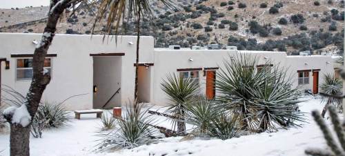 Snow-covered buildings with desert plants in the foreground, set against a mountainous landscape.
