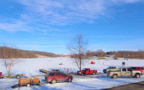 A snowy landscape with a frozen lake, surrounded by parked vehicles and a clear blue sky.