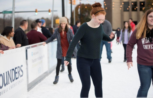 A group of people ice skating outdoors, with a focus on two young women enjoying the activity.