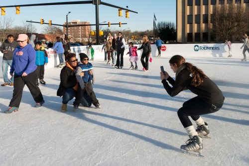 A group of people ice skating, with one person taking a photo of another on the rink.