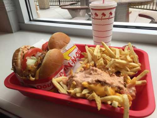 A red tray with two burgers, a serving of fries, and a drink, all placed near a window.