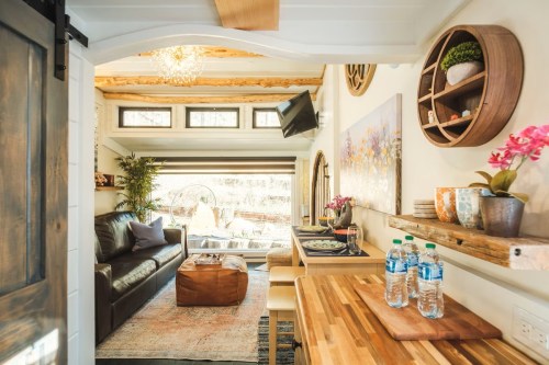 Cozy interior of a small living space with a leather sofa, wooden accents, and a view of a garden through large windows.