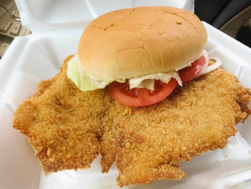 A fried chicken sandwich with lettuce and tomato, served on a bun, alongside two crispy fried chicken fillets.