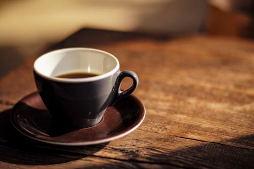A black coffee cup on a brown saucer, resting on a rustic wooden table with soft lighting.