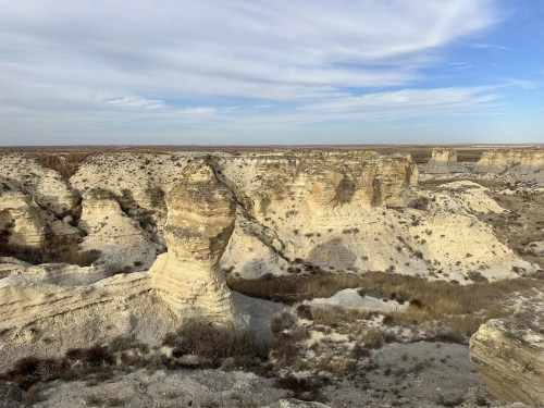 A vast landscape of eroded white rock formations and sparse vegetation under a cloudy sky.