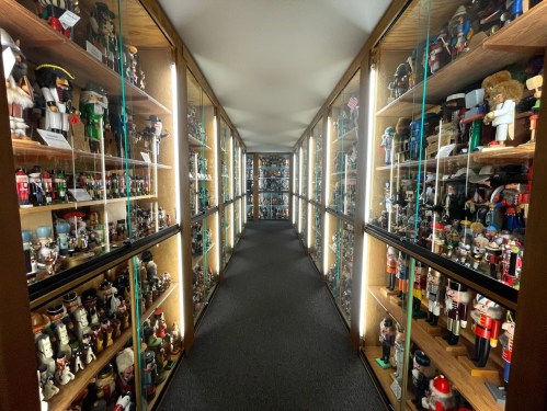 A narrow hallway lined with glass display cases filled with various nutcracker figurines.