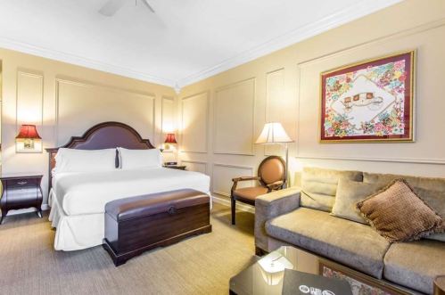 Cozy hotel room featuring a king bed, sofa, and decorative artwork on the wall. Warm lighting creates a welcoming atmosphere.