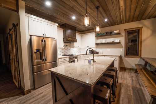 Modern kitchen with wooden ceiling, granite island, stainless steel appliances, and warm lighting.