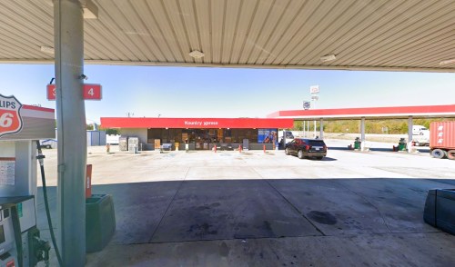 A gas station with a red roof, fuel pumps, and a convenience store, set against a clear blue sky.
