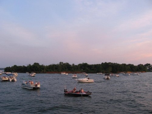 A scenic view of multiple boats on a calm lake during sunset, with people enjoying their time on the water.