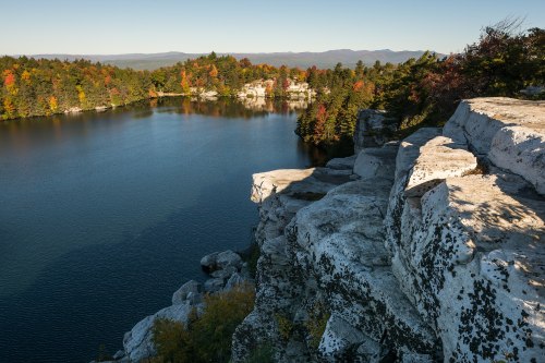 A serene lake surrounded by colorful autumn foliage and rocky cliffs under a clear blue sky.