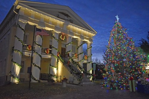 Historic building decorated for the holidays, featuring wreaths and a brightly lit Christmas tree nearby.
