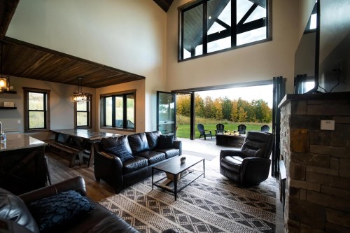 Cozy living room with large windows, leather furniture, and a view of a green outdoor space.