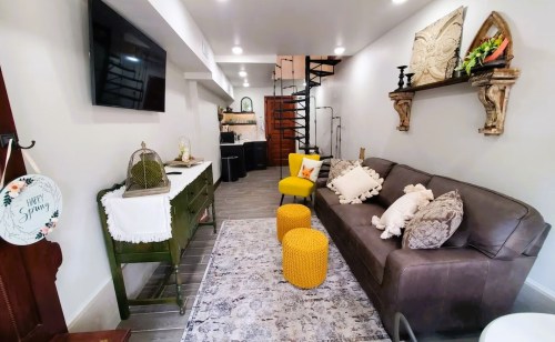Cozy living space featuring a brown sofa, yellow accents, a decorative rug, and a spiral staircase in the background.