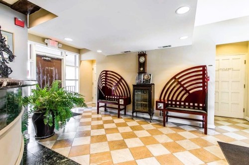 A lobby area featuring two wooden benches, a clock, and a potted fern, with a checkered tile floor.