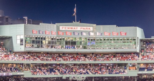 Fenway Park at night, showcasing the iconic green facade and a crowd enjoying a baseball game.