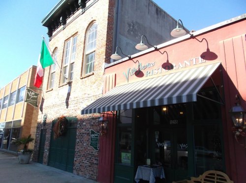 Exterior of a brick restaurant with an Italian flag, featuring a striped awning and decorative lights.