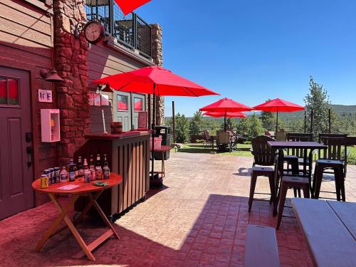 Outdoor patio with red umbrellas, a bar area, and scenic views of trees and blue sky.