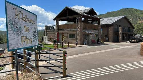 A sign reading "Welcome to Pine" in front of a rustic building surrounded by mountains and blue skies.