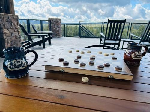 A checkers board with pieces in play, two mugs on a wooden table, and a scenic view in the background.