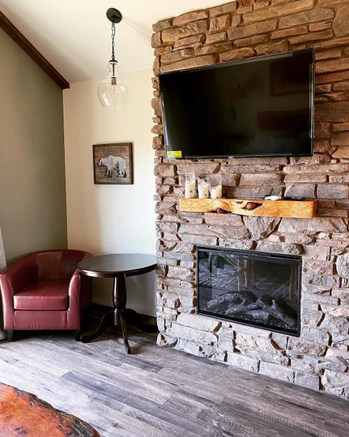 Cozy living space featuring a stone fireplace, wall-mounted TV, a red armchair, and a small round table.