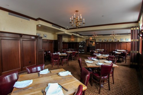 Elegant restaurant interior with wooden paneling, chandeliers, and neatly set tables.