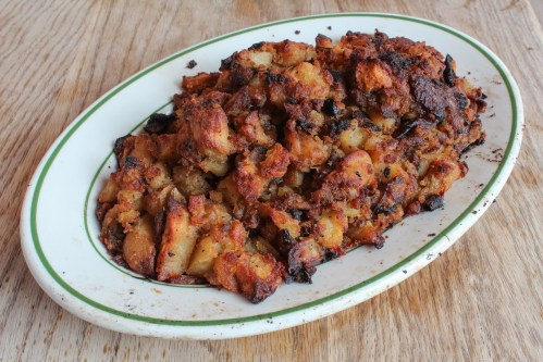 A platter of golden-brown stuffing with crispy edges, served on a white dish with a green rim, on a wooden surface.