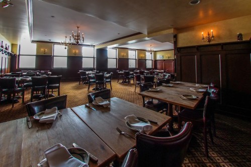 A spacious, elegantly decorated restaurant with wooden tables, leather chairs, and soft lighting.
