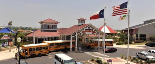 Entrance of a theme park with school buses parked outside, flags flying, and a welcoming sign.