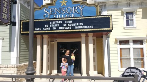 A woman stands with two children in front of the Sensory Village sign at Morgan's Wonderland.