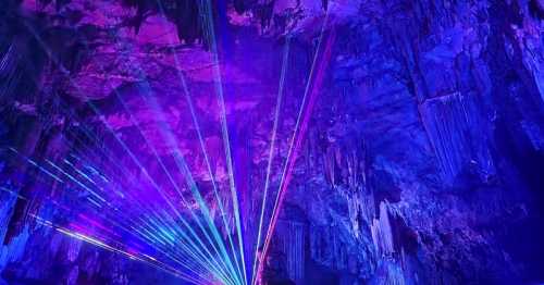 Colorful laser lights illuminate a cave's rocky interior, creating a vibrant display against the dark, textured walls.