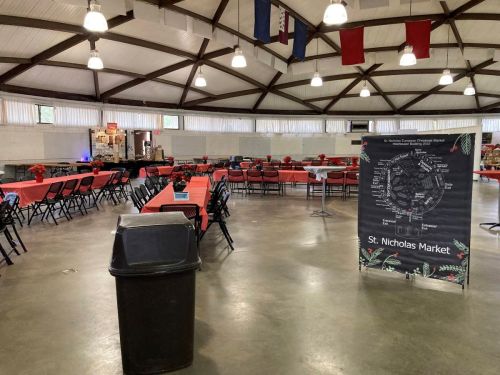 Interior of a large hall set up for an event, featuring tables with red tablecloths and a sign for St. Nicholas Market.