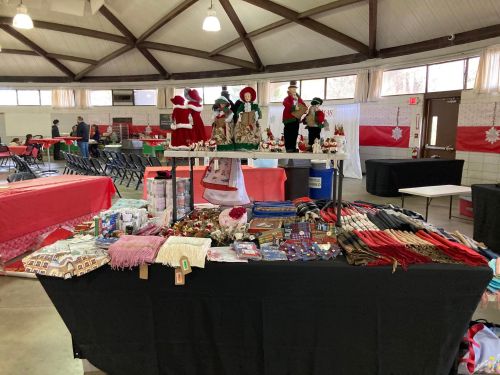 A festive indoor market with tables displaying crafts, decorations, and holiday-themed items.
