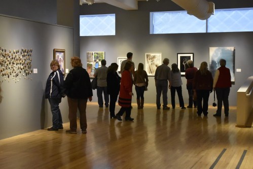 Visitors explore an art gallery, admiring various artworks displayed on the walls.