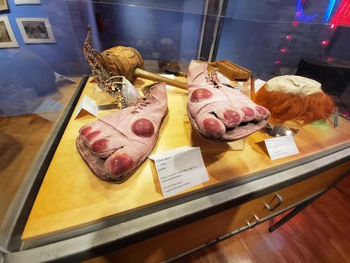 A display case featuring oversized clown shoes with exaggerated toes and a clown wig, showcasing unique theatrical props.