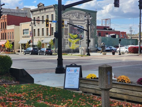 A street view featuring a café sign, colorful autumn leaves, and a mural on a building in the background.