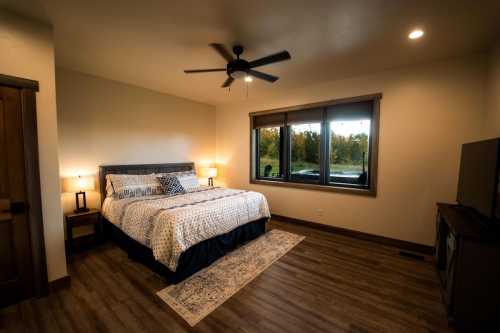 Cozy bedroom with a queen bed, wooden furniture, and large window overlooking a scenic view.