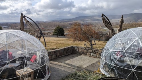 Two transparent domes with seating, overlooking a scenic landscape of hills and cloudy skies.