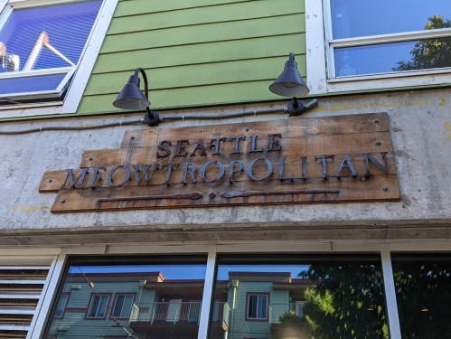Sign for "Seattle Meowtropolitan" displayed on a building exterior, featuring wooden and metal elements.