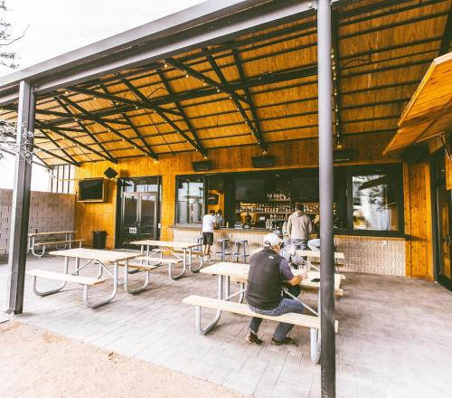 Outdoor seating area of a bar with wooden accents, featuring picnic tables and a bar counter in the background.