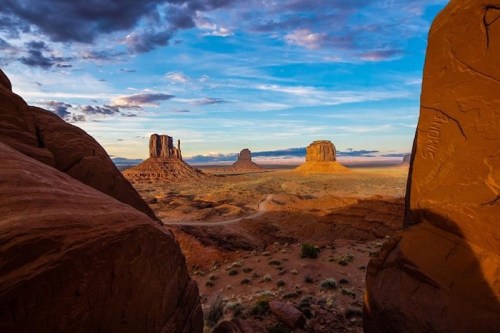 A stunning desert landscape featuring iconic rock formations under a colorful sky at sunset.