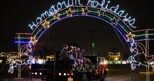 A festive archway reading "Hometown Holidays" adorned with lights, with people in Santa hats on a truck below.