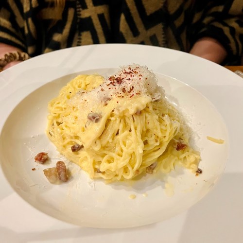 A plate of creamy pasta topped with grated cheese and red pepper flakes, served in a white bowl.