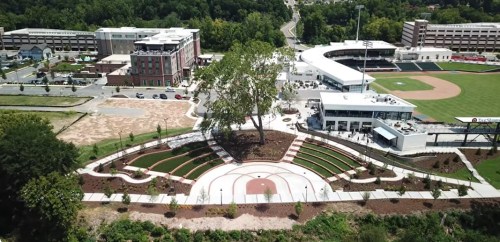 Aerial view of a park with landscaped gardens, a baseball field, and nearby buildings in a green urban area.