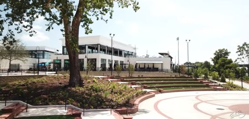 A modern building with outdoor seating, surrounded by landscaped greenery and steps, under a clear blue sky.
