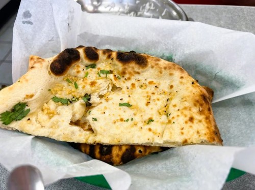 A piece of garlic naan bread with herbs, served in a basket lined with parchment paper.